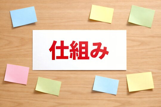 木目背景にカラフルな付箋と仕組みという赤い文字が書かれた白い紙があるビジネス素材