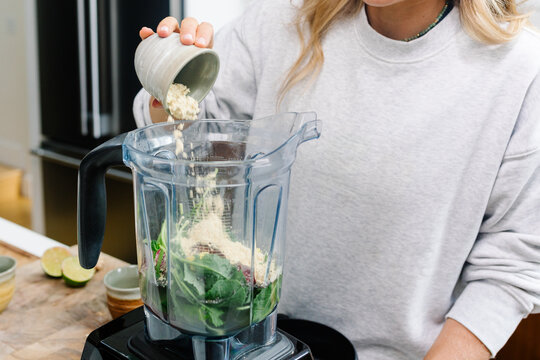 Unknown lady adding ingredients to a blender to make healthy smoothie