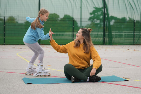 Mother coaching daughter on rollerblades during outdoor high five session