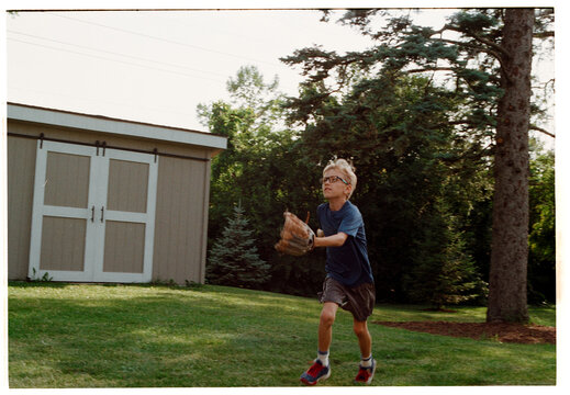 Boy Catches Baseball in Backyard With Trees in the Background