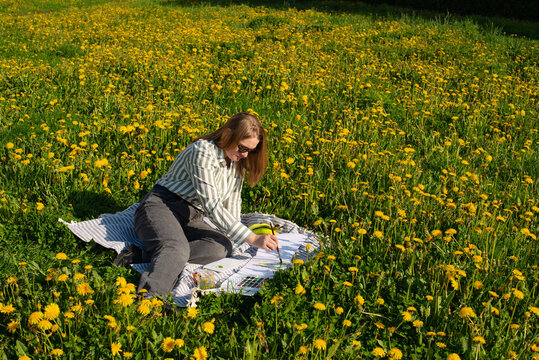 Creative artist paints in sunlit meadow filled with dandelions