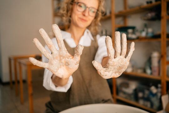Woman Working With Clay Shows Her Hands Covered in Pottery