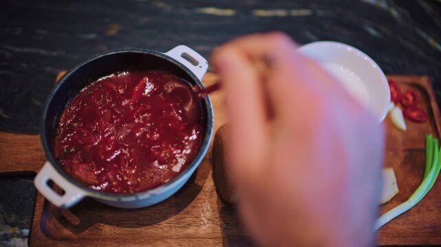 Close up of a spoon stirring borscht inside a small pot placed on a wooden board