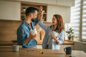 Happy couple achieving financial goals with piggy banks © Miljan Živković