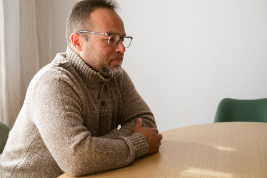 Man in a Sweater Engaged in Deep Thought at a Wooden Table