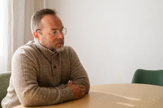 Man in Casual Sweater Sitting Thoughtfully at Round Table