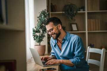 Obraz premium Man working from home on laptop, telecommuting smiling