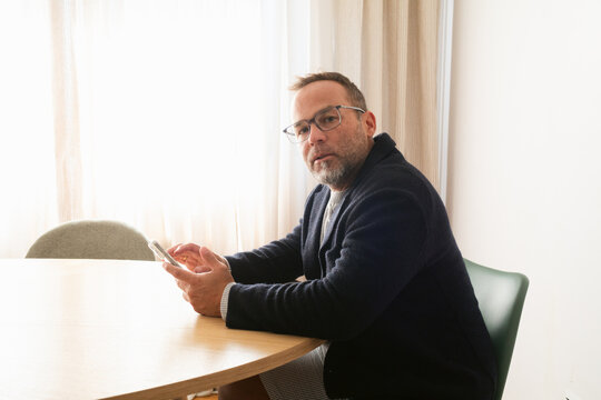 Man Sitting at a Table Using Smartphone in a Well-Lit Room