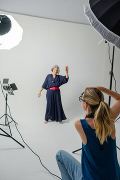 Photographer taking pictures of senior model waving in studio