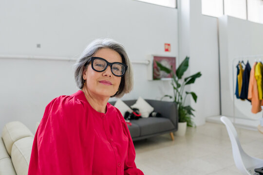 Confident senior fashion designer sitting in modern office showroom