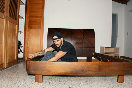 Man assembling a wooden bed frame in a minimalist bedroom