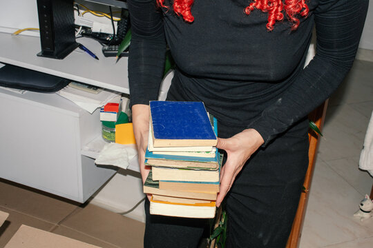 Person carrying a stack of vintage books in a workspace