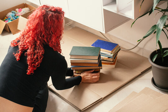 Person organizing books in a living room on a cardboard surface