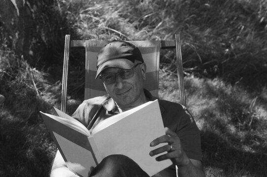 Man reading a book in a long chair.