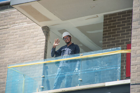 Construction worker waves from new building balcony during day