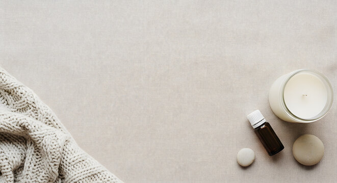 Wellness flat lay with essential oil bottle scented candle and knitted blanket on beige linen background