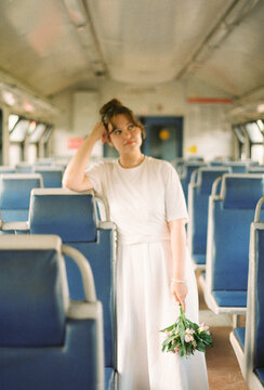 Woman in white dress holding flowers on empty train
