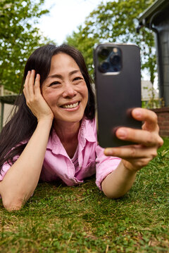 Middle aged asian woman taking selfies on grass outside