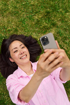 Middle aged asian woman taking selfies on grass outside