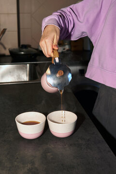 Woman serves coffee into two cups
