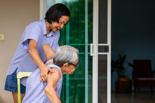 Asian daughter helping senior woman stand up at home in Thailand