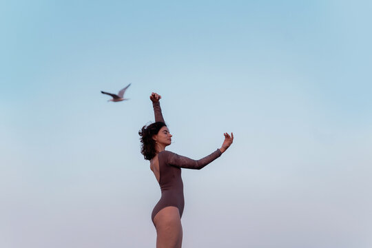 Woman Dancing Gracefully Under a Clear Blue Sky With a Bird Flying