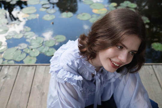 Model smiles near a tranquil pond surrounded by lily pads 