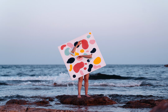 Person Holding Colorful Abstract Art Canvas by the Sea