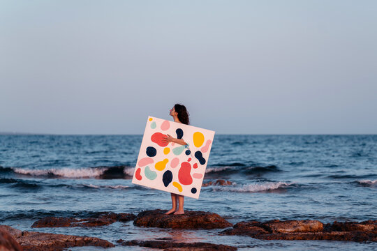 Woman Holding Colorful Abstract Art Canvas by the Sea