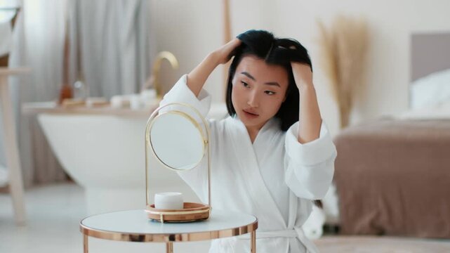 Young pretty woman making hairstyle at home, looking at mirror and fixing hair, getting ready for date at bathroom in morning, slow motion, free space