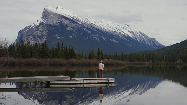 Woman standing on a pier enjoying the scenic mountain views reflecting in Vermilion Lakes in Banff National Park