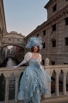Woman in blue festive dress and hat standing on a bridge
