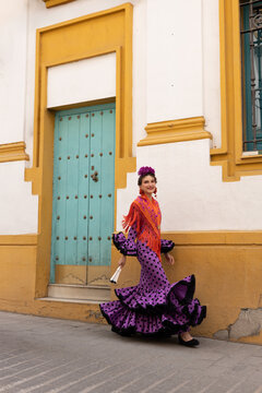 Smiling woman in vibrant flamenco outfit holding a fan outdoors