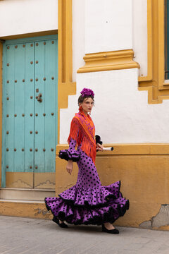 Woman in festive Spanish dress holding fan on city street