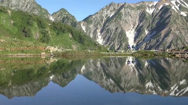 朝日を浴びた新緑の八方池と交差する登山者
