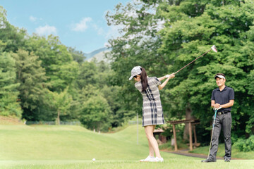 Obraz premium A male golfer teaching golf at a golf course and a female golfer hitting a tee shot