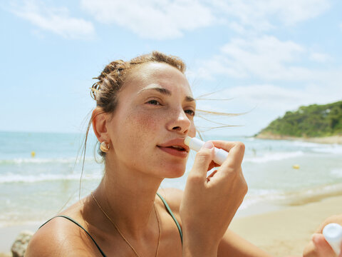 Woman Applying Lip Balm on Beach During Sunny Day