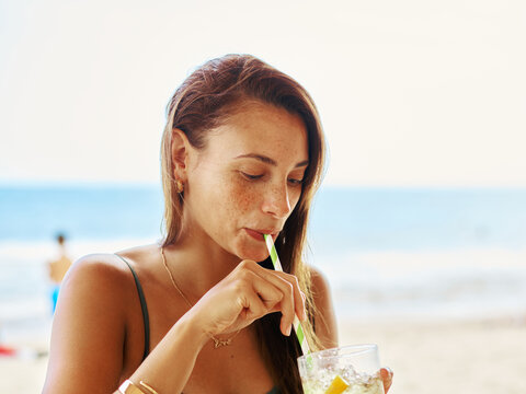 Woman Enjoying a Refreshing Drink at the Beach During Midday
