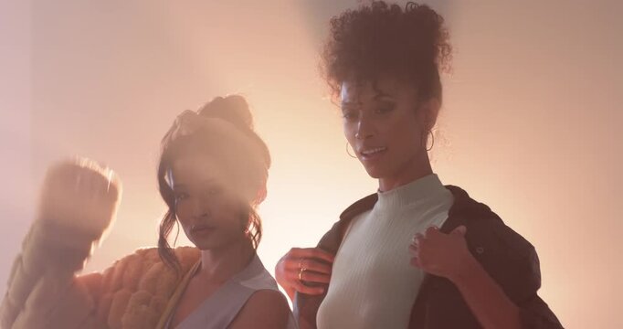 Asian woman and African American woman after photographer cue, adjusting fuzzy jacket and posing