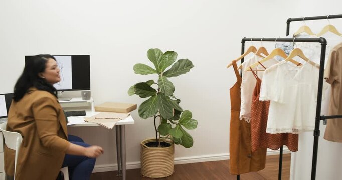 Receiving boxes from coworker, Hispanic woman sorting garments on rack to match sketches in studio