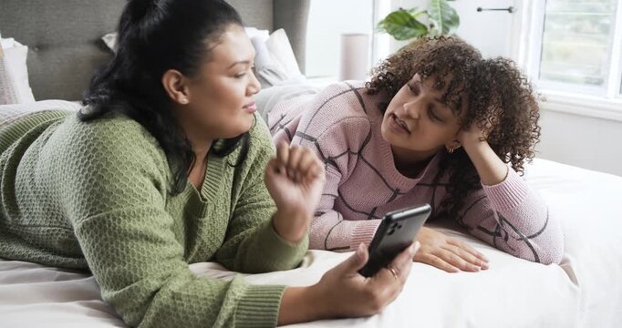 Mother and daughter lying on bed with white comforter scrolling smartphone finding surprising post