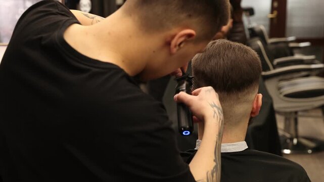 Stylist cutting man's hair with clipper in barbershop