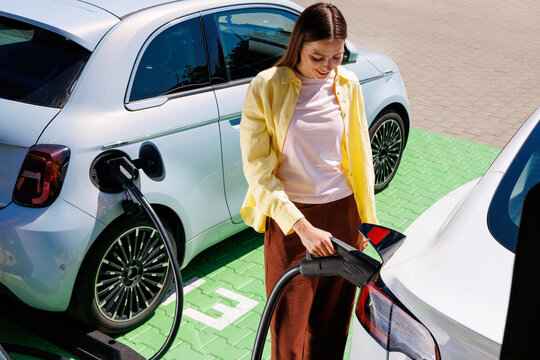 Woman Charging Electric Car at Station in Green Urban Parking Area