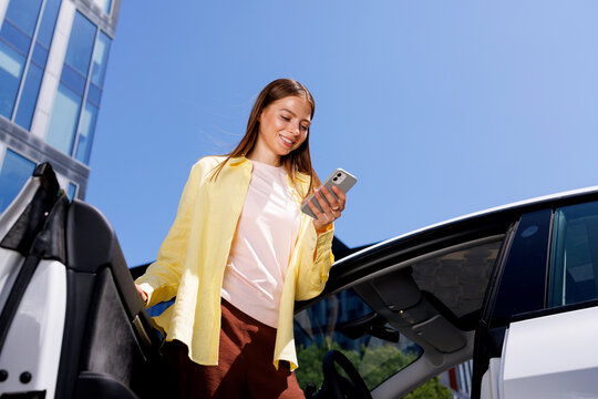 Woman Standing Beside Modern Car Using Mobile