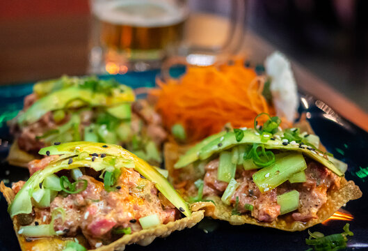 Platillo de tostadas con mariscos y especies con aguacate y cebollin encima con lineas de zanahoria sobre un plato, con cerveza en el fondo. fotografia MACRO.