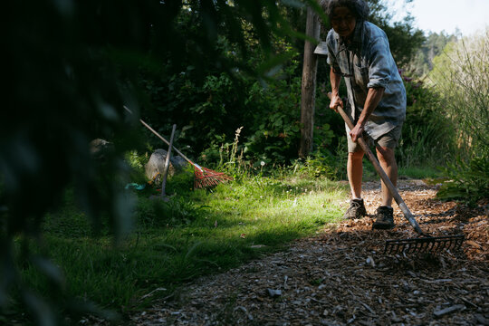 Person raking wood chips in a garden on a sunny day outdoors