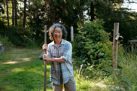 Smiling gardener in casual attire holding a rake in a sunny back