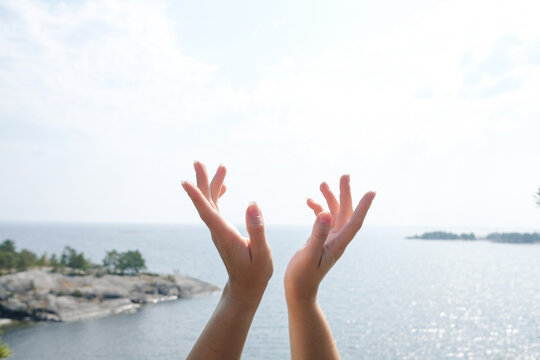 Hands Reaching Towards a Bright Sky Over Tranquil Water