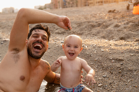 Father and son laughing together on beach during sunset