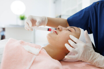 Naklejka premium A woman is getting a facial treatment with a syringe. The woman is wearing gloves and the syringe is being used to inject a substance into her face. The scene is set in a medical or spa setting 
